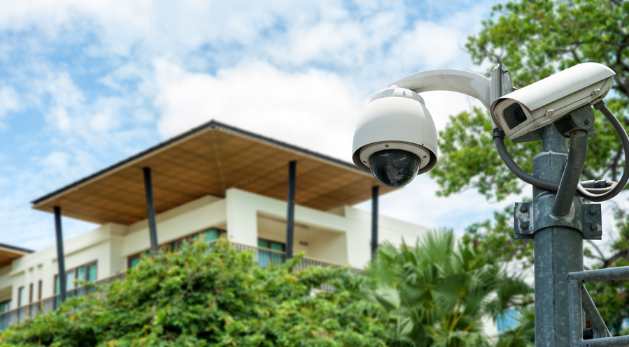 closeup of a dome and pan-tilt-zoom security camera with a commercial building in the background